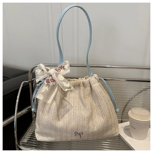 Detail of beige woven tote bag featuring embroidered lace bow and blue leather straps