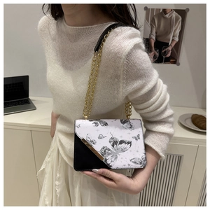 Détail d'un petit sac carré à motif papillon avec chaîne dorée porté par un mannequin