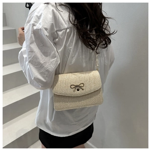 Detailed close-up of a beige straw woven handbag featuring a metal bow clasp and strap