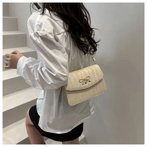 Detail of beige woven crossbody bag with gold bow clasp worn with French chic outfit