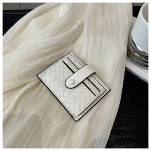 Détail d'un porte-cartes en cuir tressé blanc avec bouton pression sur soie