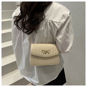Detail of beige straw crossbody bag with golden bow clasp on white stairs