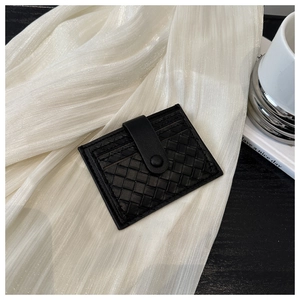Détail d'un porte-cartes en cuir tressé noir avec bouton pression sur tissu plissé