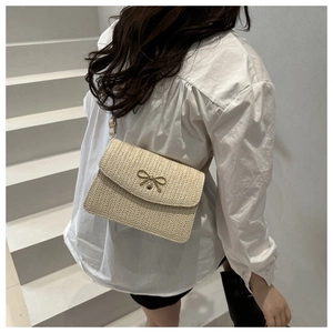 Detail of beige woven crossbody bag featuring a golden bow metal accessory and fine texture