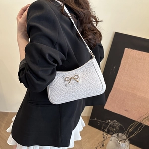 White woven crescent shoulder bag with golden bow clasp shown on a fashion model