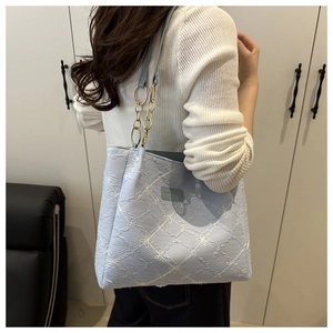 Detail of light blue tote bag with white floral embroidery and gold chain strap