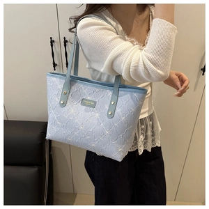 Detail of light blue tote bag featuring white floral embroidery and gold metal hardware