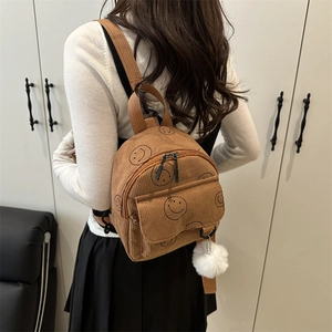 Brauner Cord-Rucksack mit Smiley-Print und Plüschball-Anhänger getragen vom Modell