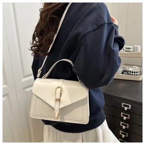 Détail d'un sac bandoulière blanc en similicuir avec boucle dorée porté par un mannequin
