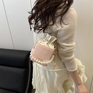 Pink snake pattern bucket bag with pearl handle and chain strap on a white sofa