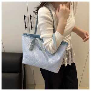 Close-up of light blue striped tote bag with white floral embroidery and leather handles