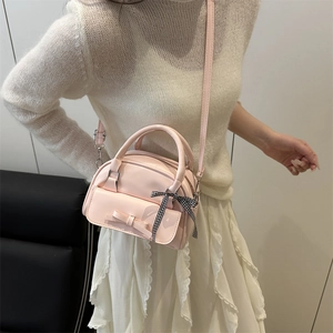 Pink crossbody handbag with leather bow and plaid ribbon shown on a shoulder