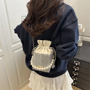 Grey snake-print bucket bag with pearl handle and gold chain strap worn by a model