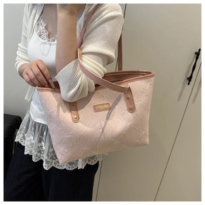 Detail of light pink tote bag featuring embossed bow patterns and metal brand nameplate