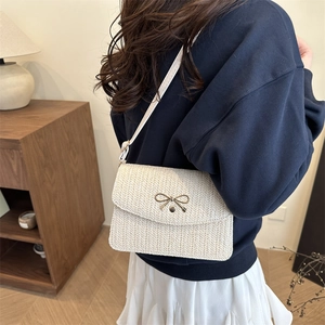 Chic cream woven crossbody bag with golden bow clasp shown on model in home setting