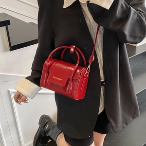 Glossy burgundy leather handbag with top handles and shoulder strap shown on model