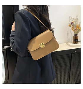 Close-up of a brown leather shoulder bag with gold metal buckle on a navy blue blazer