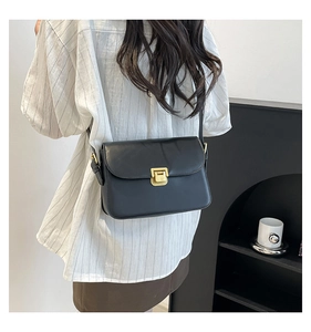 Detail of a minimalist black leather crossbody bag with a gold square clasp on a model