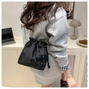 Black drawstring bucket bag with floral texture and gold chain on model in home setting