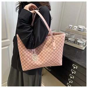 Side view of a pink monogram tote bag with gold M pendant worn by a model in a casual setting