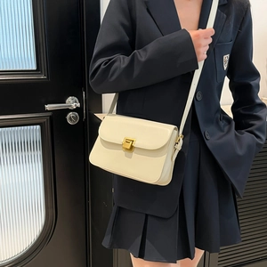 Chic beige crossbody square bag with gold metal clasp worn by a model in a black blazer