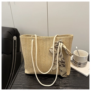 Detail of woven straw tote bag with braided handles and decorative vintage chain print scarf