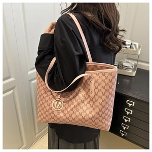 Close-up of pink tote bag with brown M pattern and a gold metal logo pendant detail