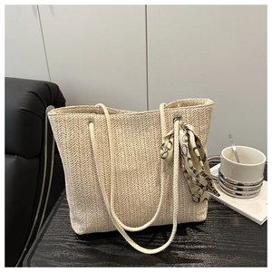 Close-up of woven straw tote bag with herringbone texture and decorative printed silk scarf