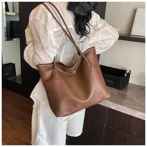 Detail of a brown pebble leather tote bag with a metal plaque and slim shoulder straps