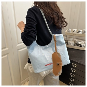 Detail of light blue denim tote bag with cartoon dog embroidery and brown leather accessory