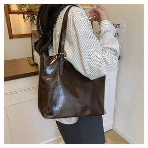 Deep brown high-gloss oil wax leather tote bag shown on shoulder in stylish cafe setting