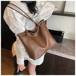 Brown lychee grain leather tote bag with silver buckle worn on shoulder by a model