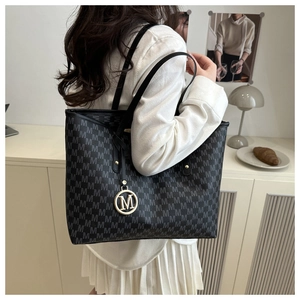 Detail of black tote bag with gray M letter print and gold circular metal pendant