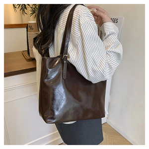Detail of dark coffee oily leather tote bag showing glossy texture on model shoulder