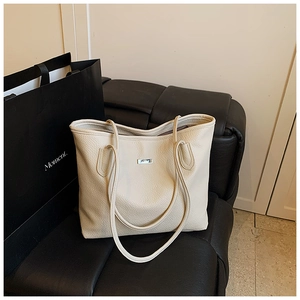 Close-up of the pebbled leather texture and silver logo plaque on the beige tote bag