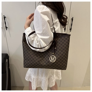 Detail of large tote bag with brown letter print and metallic M pendant on shoulder