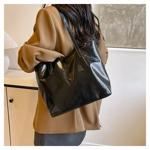 Detail of glossy black faux leather tote bag showing reflective surface and long straps