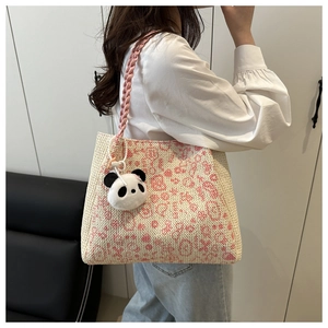Detail einer handgewebten Strohtasche mit rosa Häkelblumen und süßem Pandabär-Anhänger
