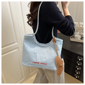 Detail of light blue denim tote bag with dog embroidery and brown leather charm accessory
