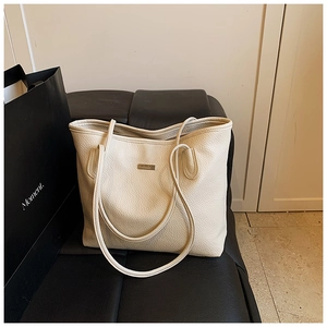 Close-up of cream lychee grain leather tote bag with metal logo on a black bench