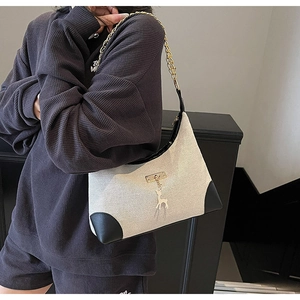Detail of canvas shoulder bag with black leather trim, deer charm and gold chain strap