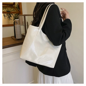 Detail view of white glossy faux leather tote bag worn on shoulder in a cafe setting