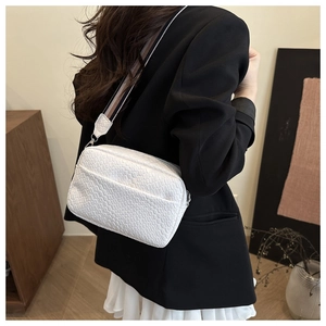Detail of white woven crossbody bag with striped shoulder strap worn by a model