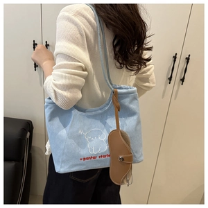Detail of light blue denim tote bag featuring dog embroidery and leather glasses holder