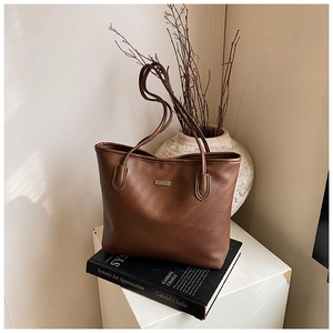 Detailed macro view of the brown lychee pattern leather tote bag with metal logo plate