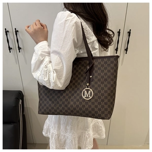 Detail of large brown tote bag with M-pattern print and gold logo charm on white dress