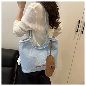 Detail of light blue denim tote bag with puppy embroidery and brown leather charm