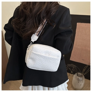 Detail of white textured square crossbody bag featuring a stylish striped wide shoulder strap
