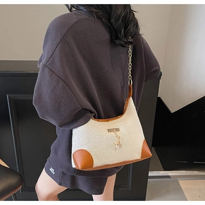 Detail of canvas shoulder bag with brown leather trim, gold chain, and elk charm