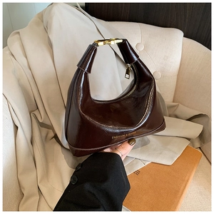 Détail de la texture en cuir marron foncé brillant et ferrures dorées du sac à main